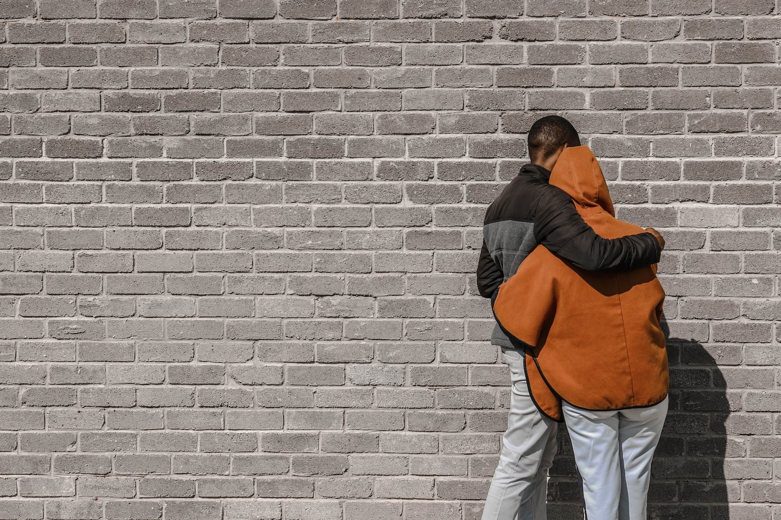 Two people hugging in front of a brick wall