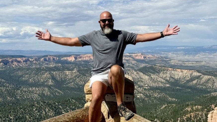 man sitting on fence with expansive view behind him