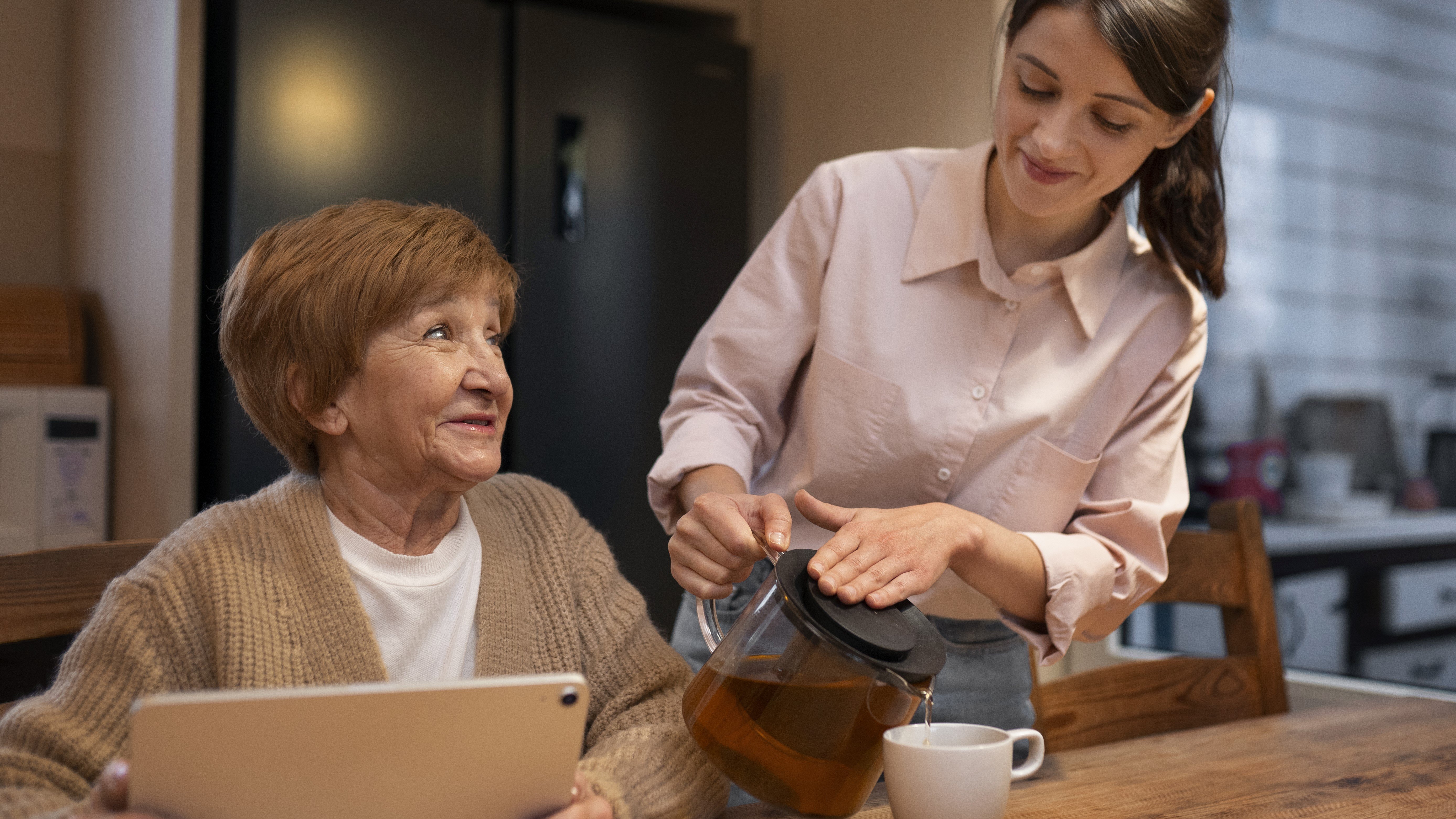 senior woman at computer with caregiver pouring coffee