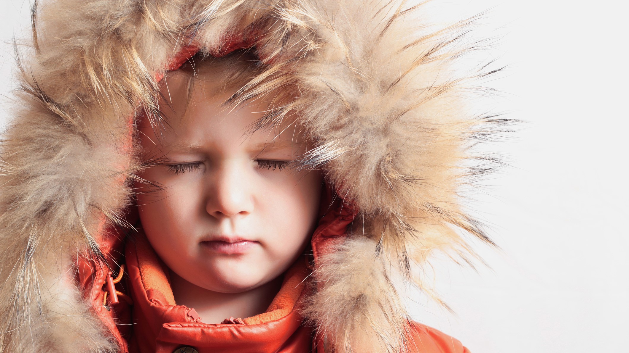 Scared child with eyes closed in a parka