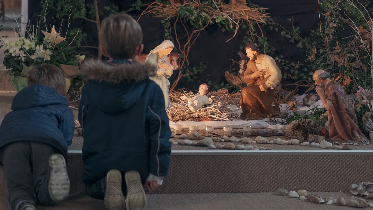 Young kids kneel before a nativity creche